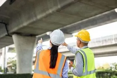 construction workers stand under a concrete bridge